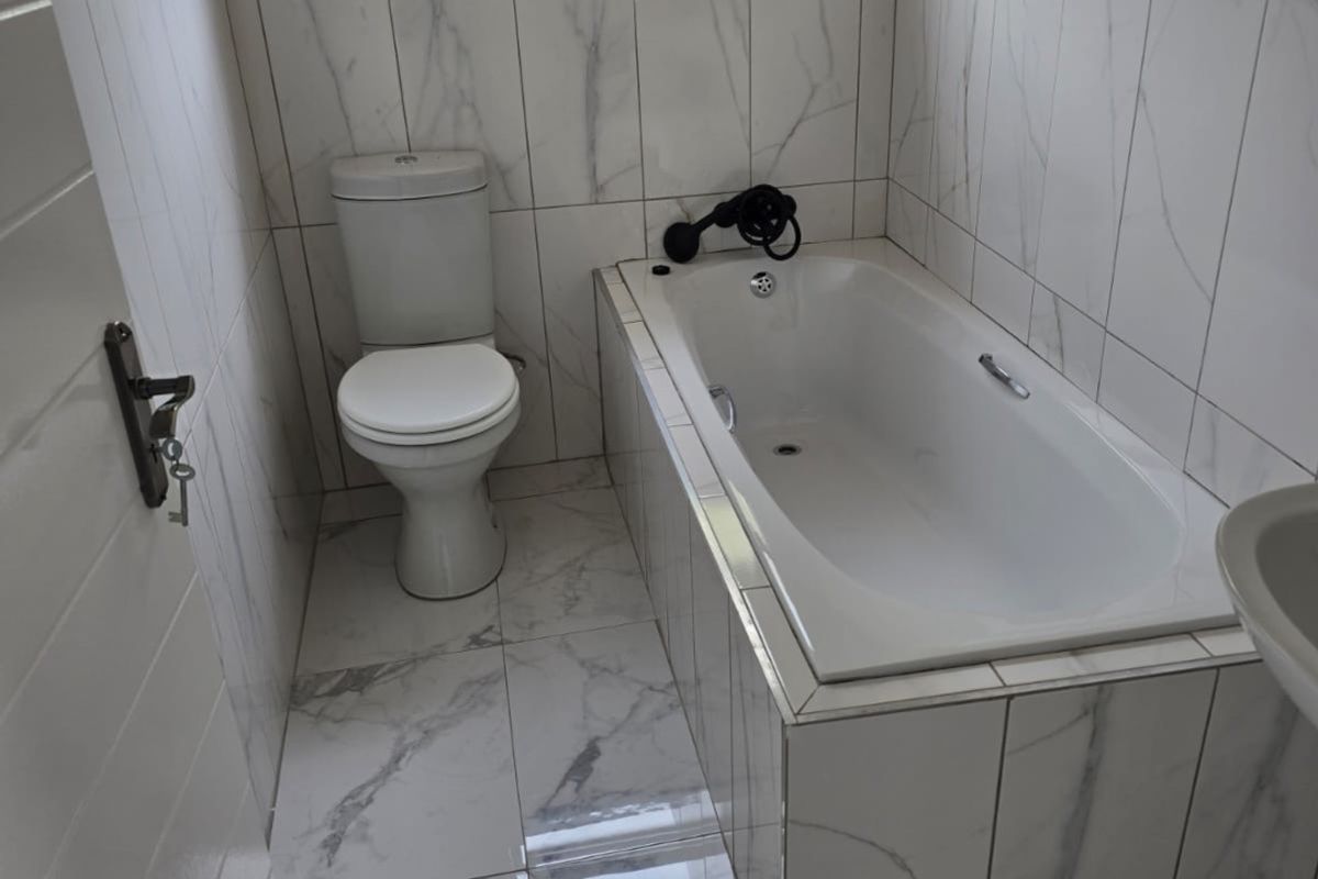A clean, modern bathroom featuring marble-look tiled walls and floors, a built-in bathtub, and a standard toilet.
