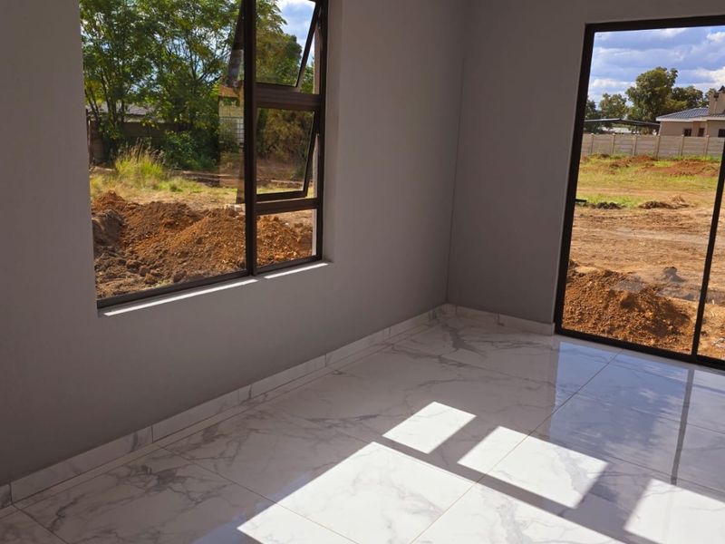 A bright, empty living area featuring modern marble-look floor tiles, aluminium window frames, and a sliding glass door leading to the exterior.