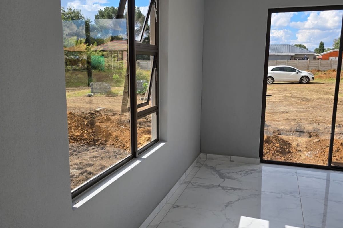 A bright, modern living area featuring high-quality marble-look floor tiles, sleek aluminium window frames, and a sliding glass door leading to the exterior.