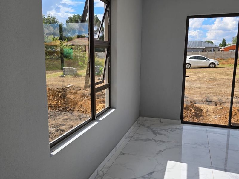 A bright, modern living area featuring high-quality marble-look floor tiles, sleek aluminium window frames, and a sliding glass door leading to the exterior.