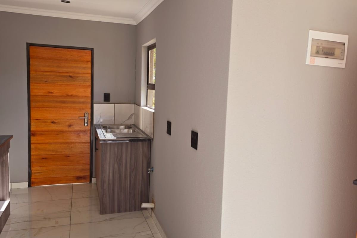 A compact, modern kitchen area featuring tiled floors, a built-in sink unit, and neutral grey walls, presenting a clean and functional space.