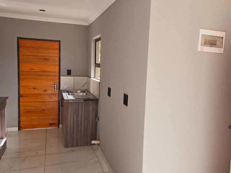 A compact, modern kitchen area featuring tiled floors, a built-in sink unit, and neutral grey walls, presenting a clean and functional space.