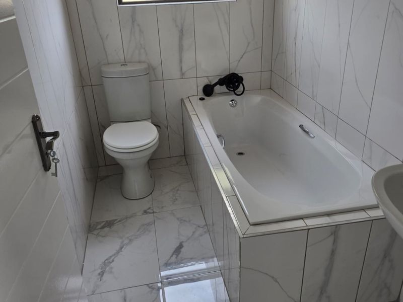 A clean, modern bathroom featuring marble-look tiled walls and floors, a built-in bathtub, and a standard toilet.