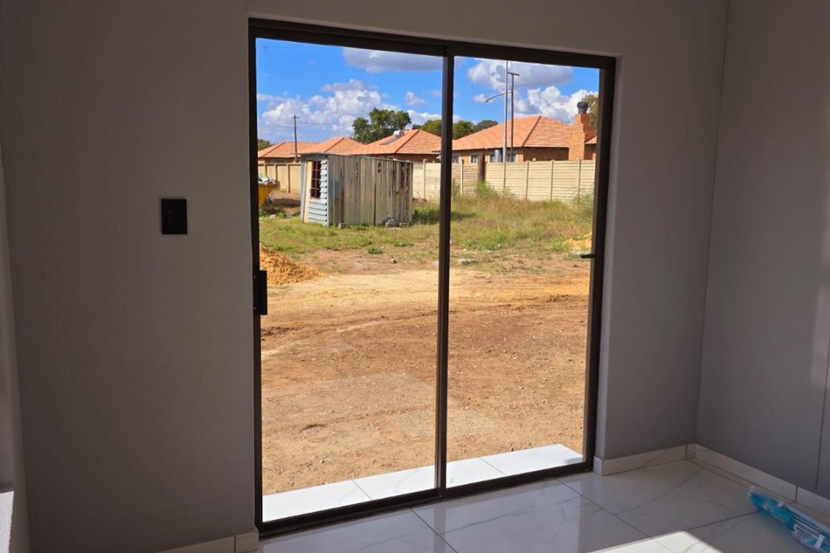 A bright, empty living area featuring modern marble-look floor tiles, recessed lighting, and a large sliding glass door opening to the rear yard.