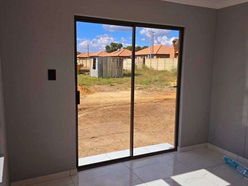 A bright, empty living area featuring modern marble-look floor tiles, recessed lighting, and a large sliding glass door opening to the rear yard.