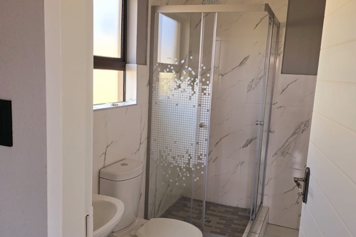 A compact bathroom featuring a shower enclosure, toilet, and wash basin with marble-look wall tiling and tiled flooring.