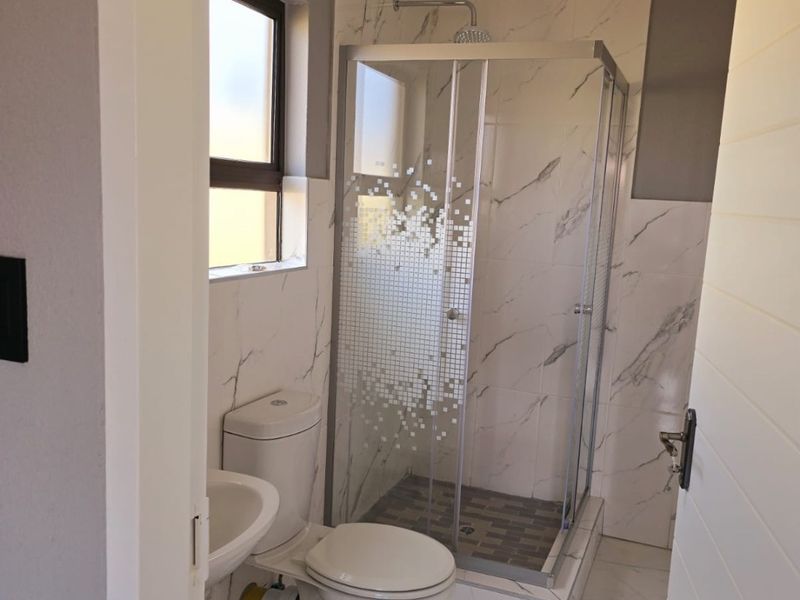 A compact bathroom featuring a shower enclosure, toilet, and wash basin with marble-look wall tiling and tiled flooring.