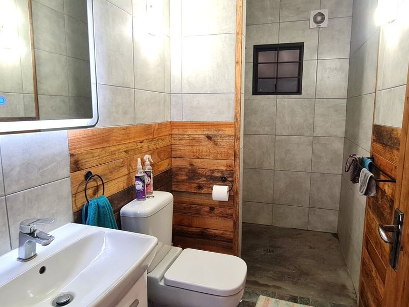 Modern bathroom featuring a vanity basin, illuminated mirror, toilet, and a walk-in shower area with a mix of tiled and timber-clad walls.