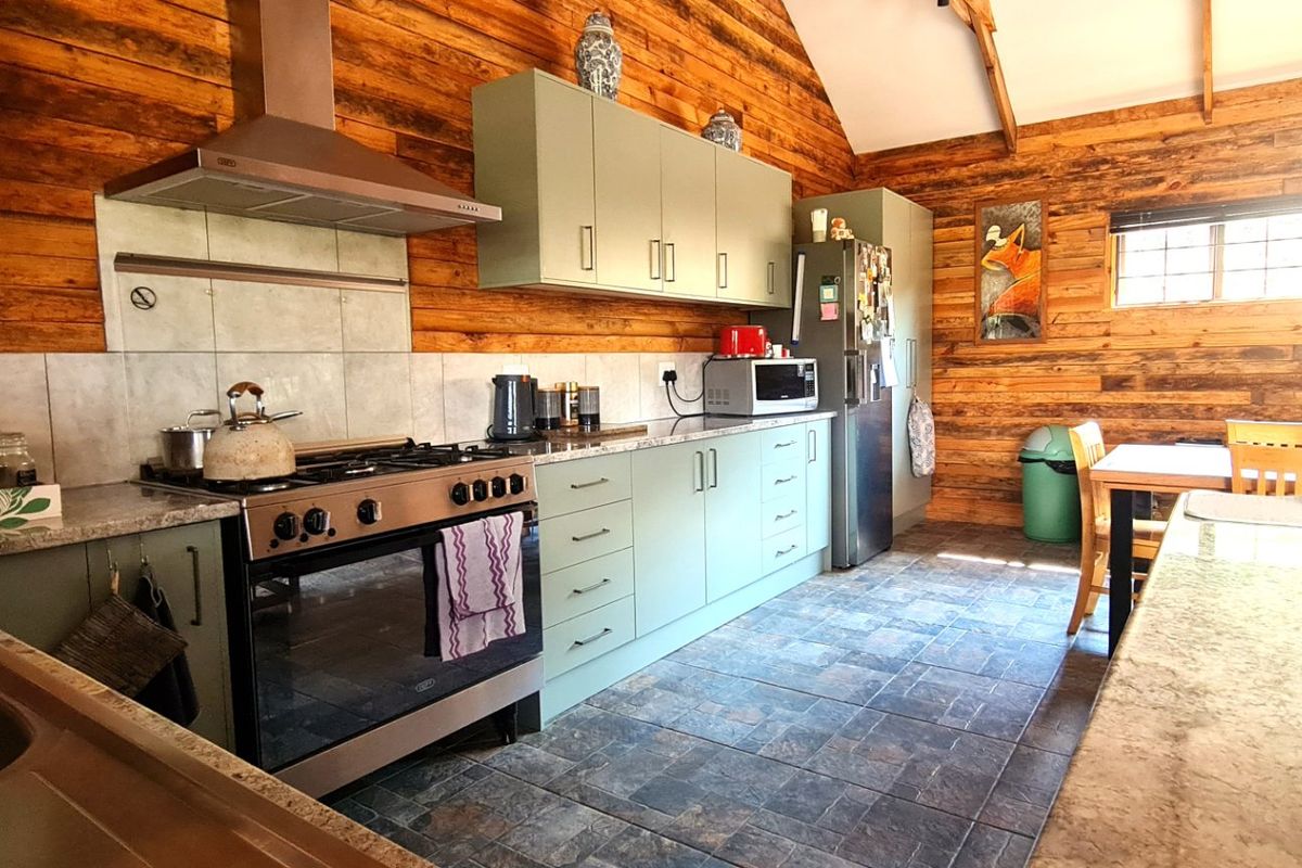 Rustic kitchen featuring timber wall cladding, exposed rafters, stone countertops, and modern cabinetry with a stainless steel gas stove and extractor fan.