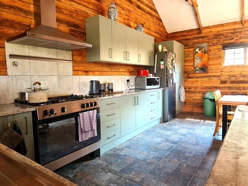 Rustic kitchen featuring timber wall cladding, exposed rafters, stone countertops, and modern cabinetry with a stainless steel gas stove and extractor fan.