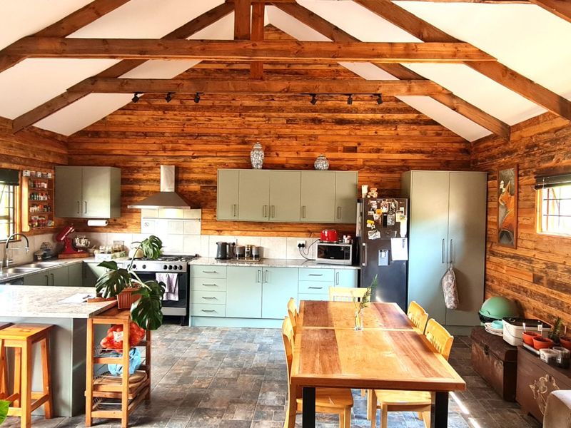 Spacious open-plan kitchen and dining area featuring rustic timber wall cladding, exposed roof trusses, and modern fitted cabinetry with integrated appliances.