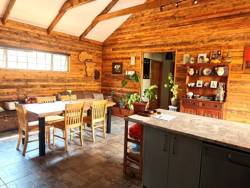Spacious open-plan living and dining area featuring vaulted ceilings with exposed timber beams, rustic timber wall cladding, and a modern kitchen island with granite countertops.