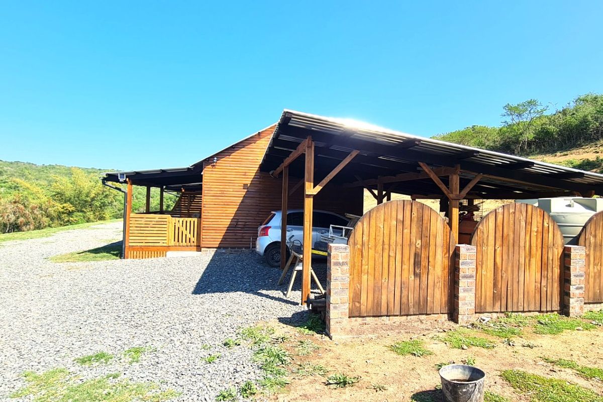Rear view of a timber-clad farm building featuring a covered carport area, brick-based timber fencing, and an integrated water storage tank.