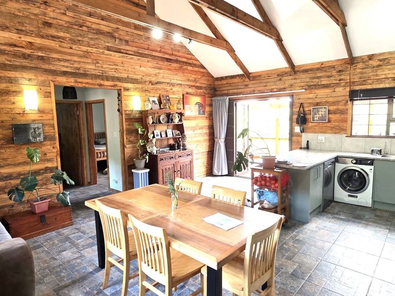 Open-plan living and kitchen area featuring rustic timber wall cladding, exposed ceiling beams, tiled flooring, and a functional kitchen with built-in appliances.