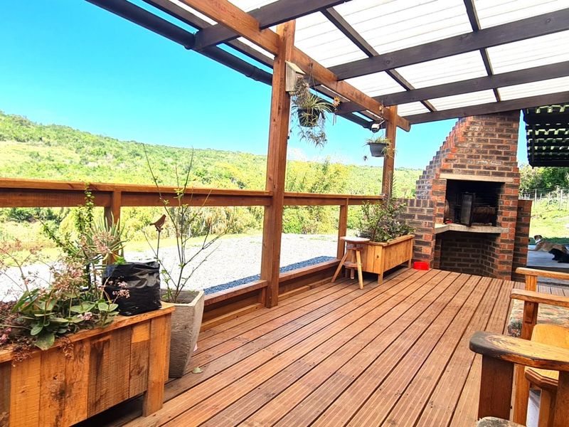 A spacious timber deck patio featuring a built-in brick fireplace, covered pergola, and scenic views of the surrounding landscape.