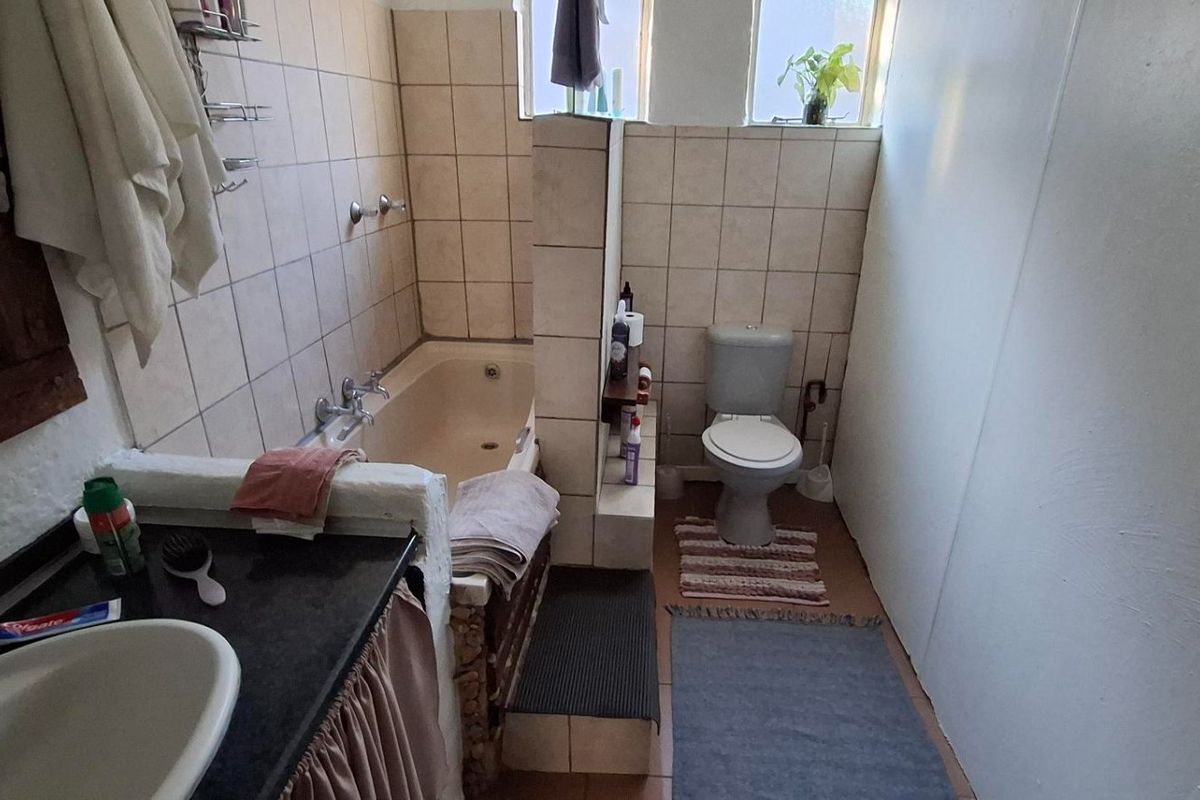 A functional bathroom featuring a built-in bathtub, toilet, and vanity basin with tiled finishes throughout.