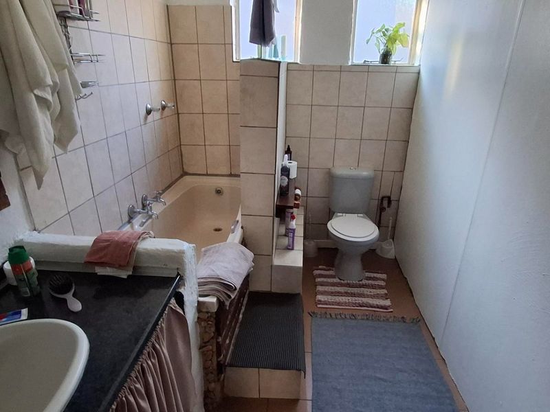 A functional bathroom featuring a built-in bathtub, toilet, and vanity basin with tiled finishes throughout.