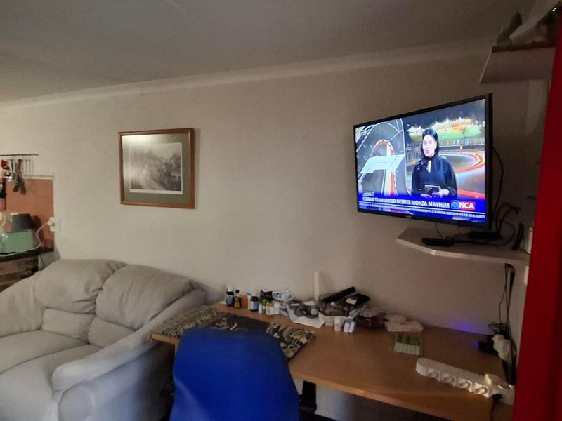 Open plan living area featuring a brick-based kitchen counter with granite top and a wall-mounted television setup.