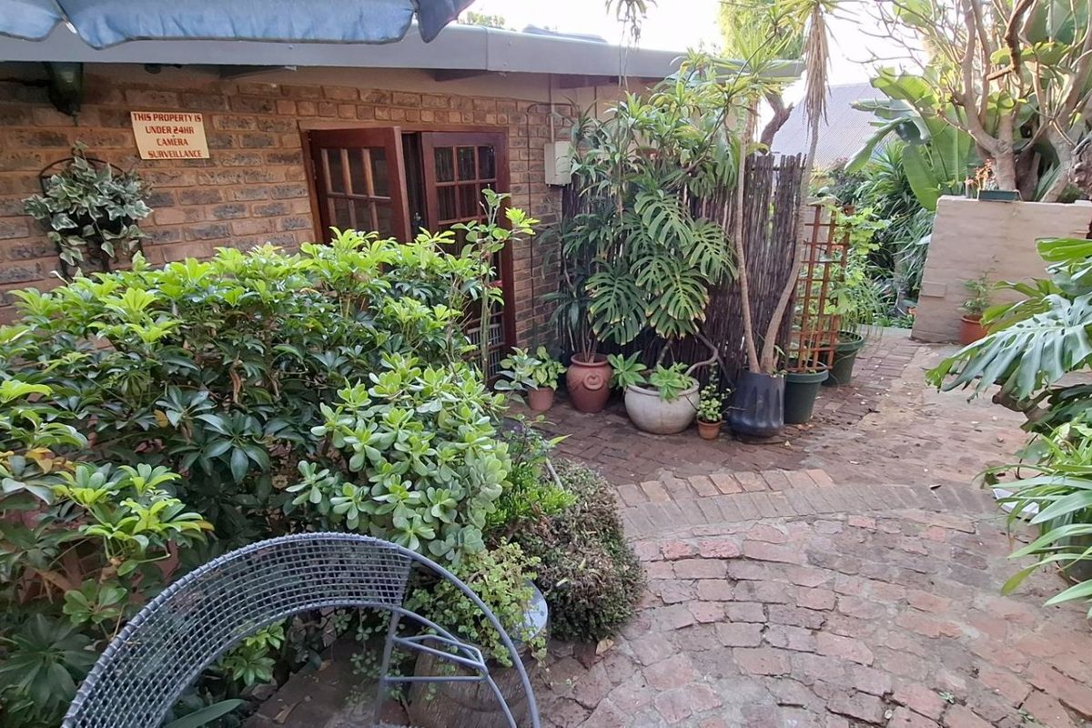 A private rear garden area featuring brick paving, established greenery, and direct access to the home through timber-framed doors.
