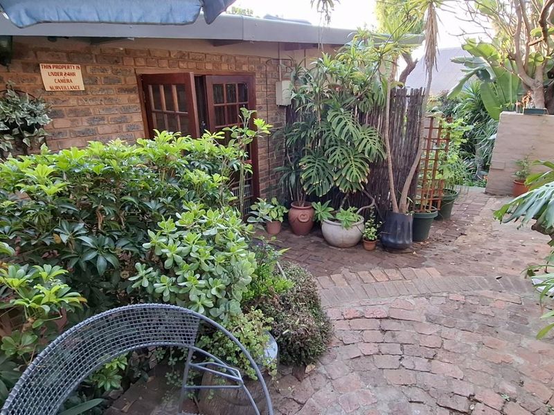 A private rear garden area featuring brick paving, established greenery, and direct access to the home through timber-framed doors.