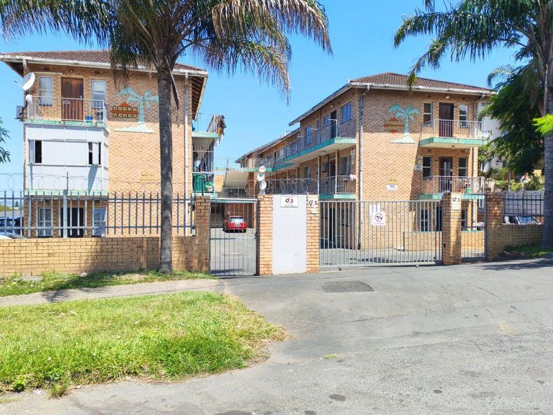 Front elevation of the Green Acres apartment complex featuring brick construction, security fencing, and multiple balconies.