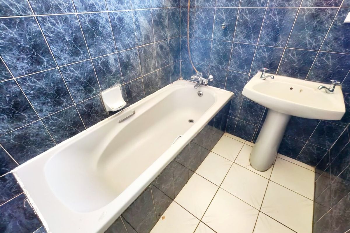 A dated bathroom featuring a standard bathtub, pedestal basin, and dark blue marble-effect wall tiles with white floor tiling.