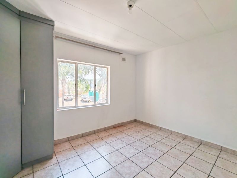 A bright, empty bedroom featuring neutral tiled flooring and a built-in cupboard, offering a clean canvas for personalization.