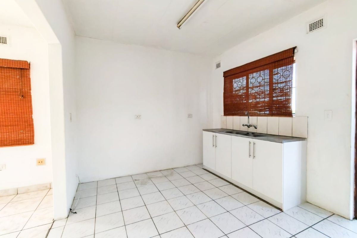 A compact, empty kitchen area featuring white built-in cabinetry, a stainless steel sink, tiled flooring, and a tiled splashback.