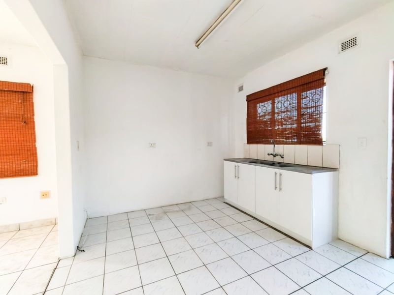 A compact, empty kitchen area featuring white built-in cabinetry, a stainless steel sink, tiled flooring, and a tiled splashback.