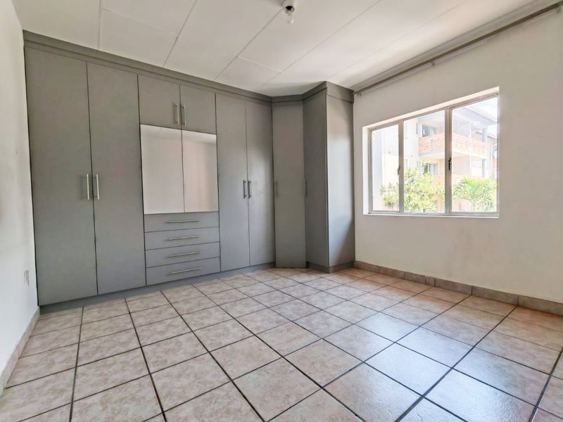 An empty bedroom featuring built-in grey cupboards, tiled flooring, and a large window allowing natural light.