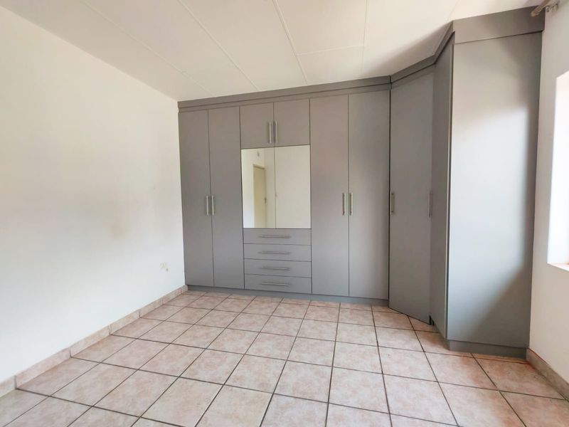 A clean, empty bedroom featuring neutral tiled flooring and extensive built-in grey cabinetry with integrated mirror and drawer storage.