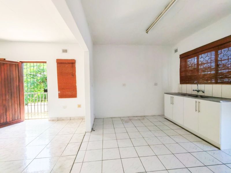 An open-plan kitchen and living area featuring white cabinetry, tiled flooring, and direct access to an outdoor space through a security gate.