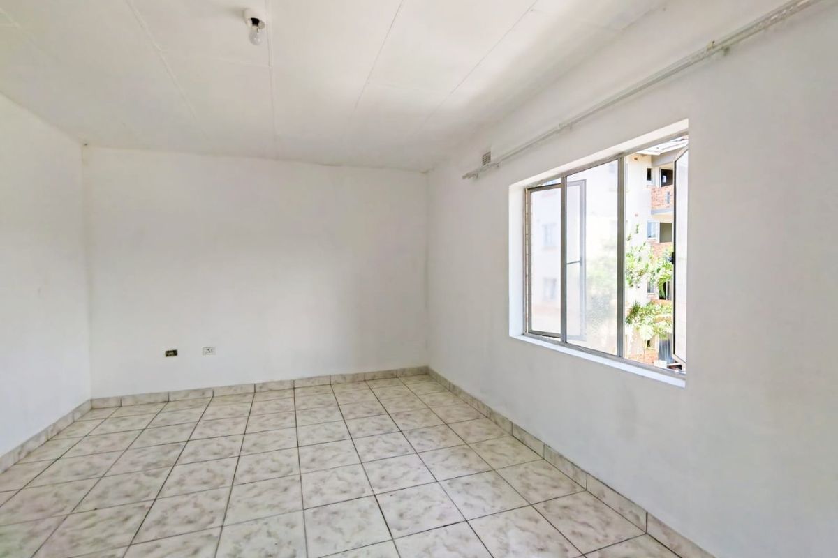 An empty bedroom featuring tiled flooring and aluminium window frames, offering a blank canvas for renovation or interior design.
