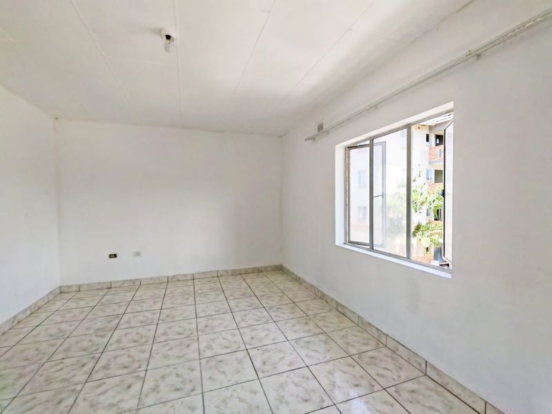 An empty bedroom featuring tiled flooring and aluminium window frames, offering a blank canvas for renovation or interior design.