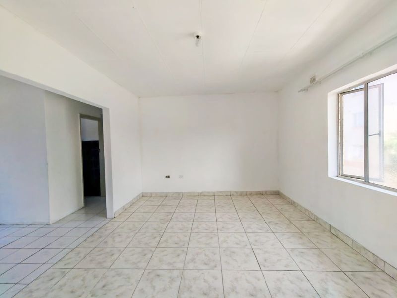 A bright, empty living room featuring neutral tiled flooring and a large window, providing a clean canvas for interior design.