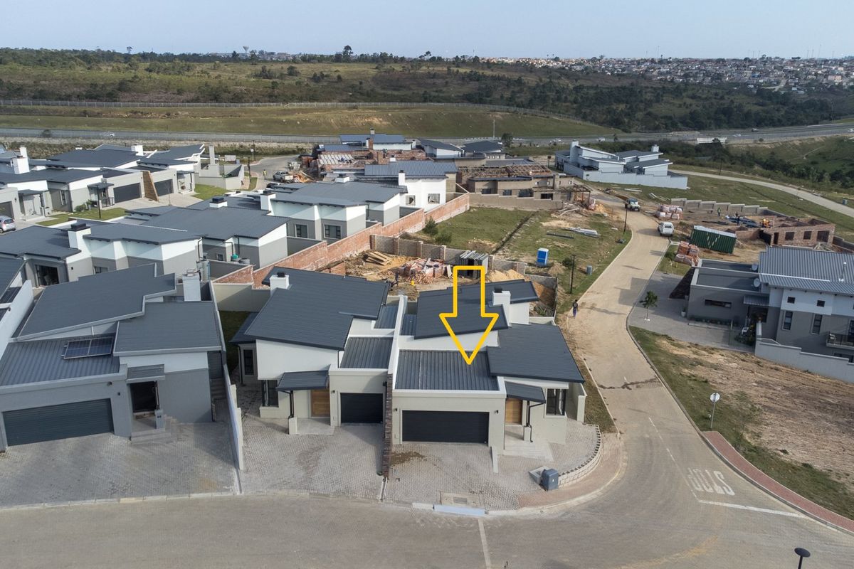 Aerial view of a modern residential property within a housing estate, featuring a metal roof, paved driveway, and attached garage.