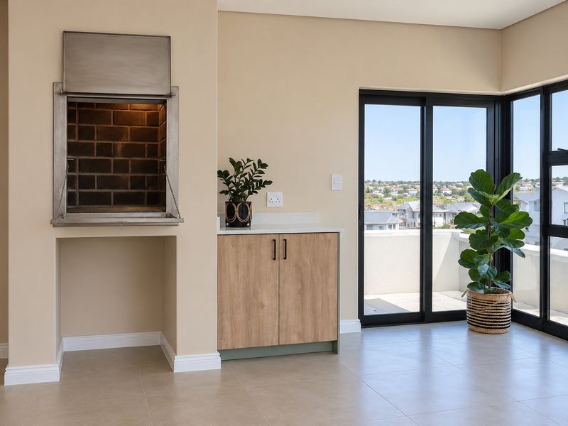 A modern covered balcony featuring a built-in braai, sleek cabinetry with stone countertops, and large sliding glass doors offering expansive views.