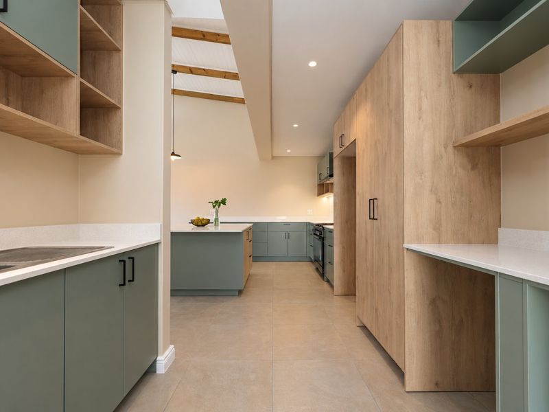 Modern kitchen featuring sage green and wood-grain cabinetry, stone countertops, a central island, and exposed timber ceiling beams in a bright, open-plan layout.
