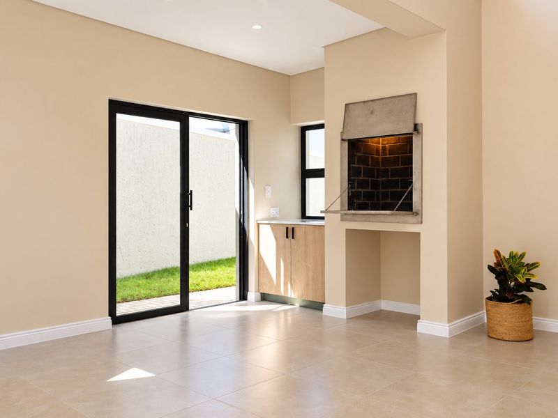A modern, empty indoor entertainment area featuring a built-in braai, tiled floors, and sliding glass doors leading to the garden.