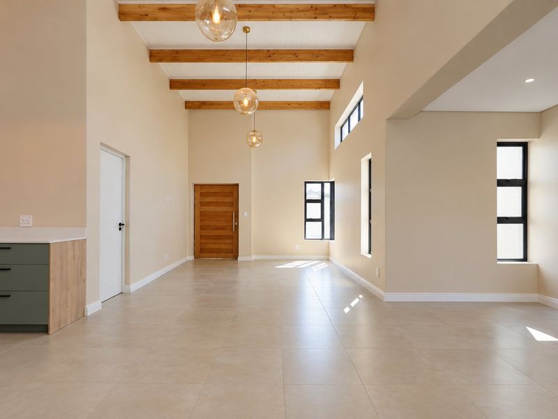 Spacious open-plan living area featuring high ceilings with exposed timber beams, large windows, tiled flooring, and a modern kitchen corner.