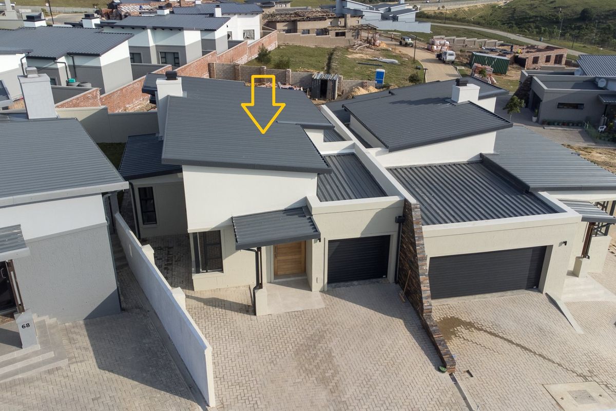 Aerial view of a modern residential property featuring a metal roof, paved driveway, double garage, and stone cladding accents in a suburban estate setting.