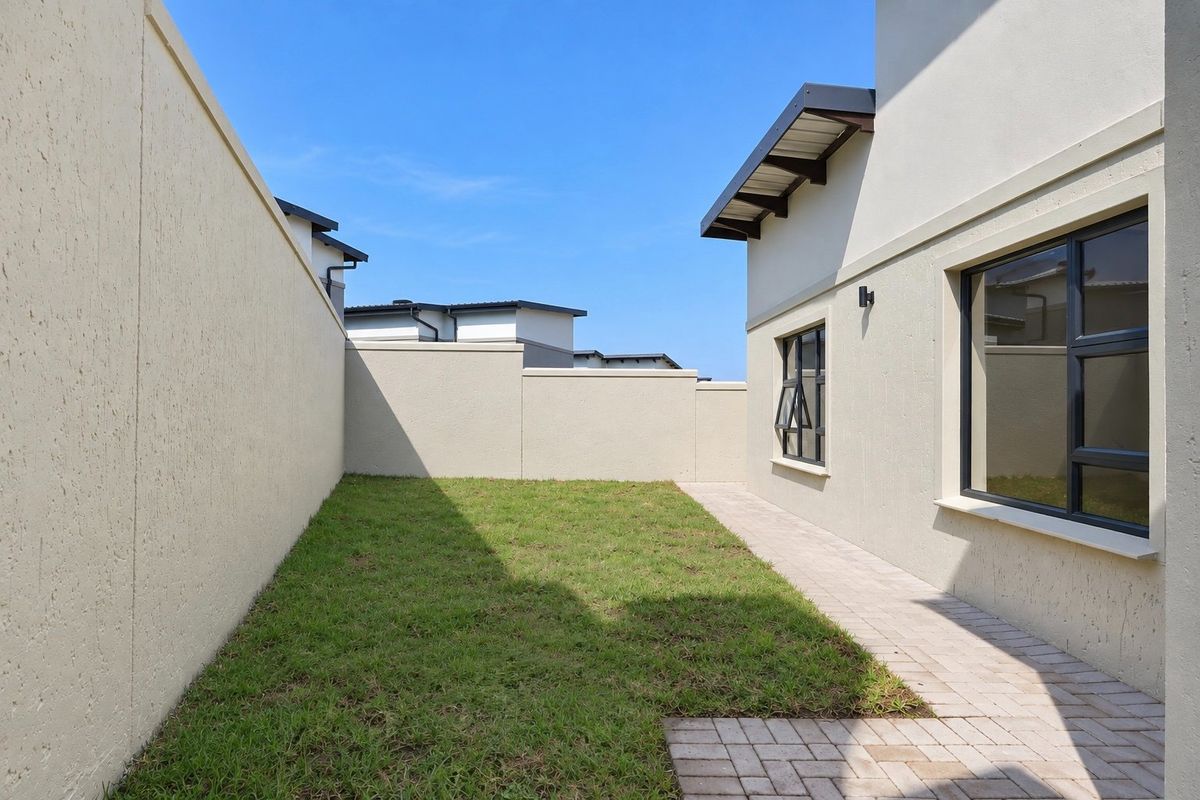 A well-maintained rear garden area featuring a paved walkway, manicured lawn, and high boundary walls for privacy.