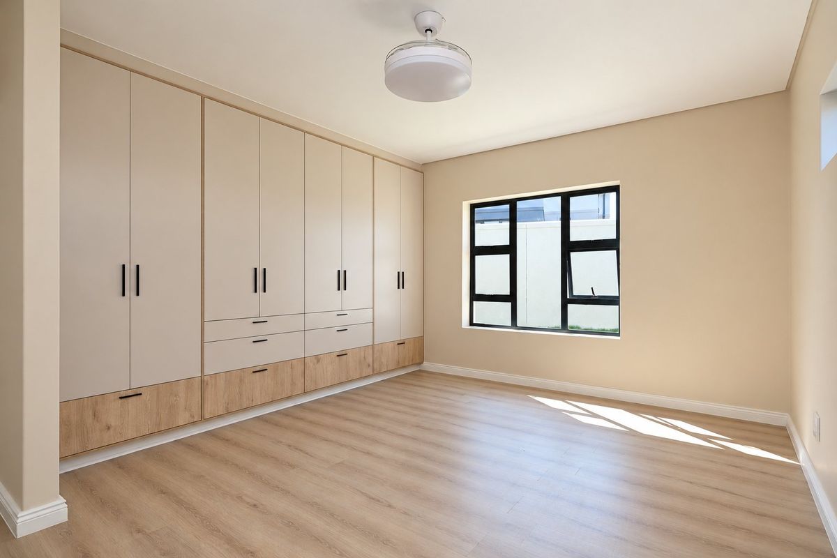 A bright, modern bedroom featuring extensive built-in cabinetry, light wood-look laminate flooring, and a contemporary ceiling fan.