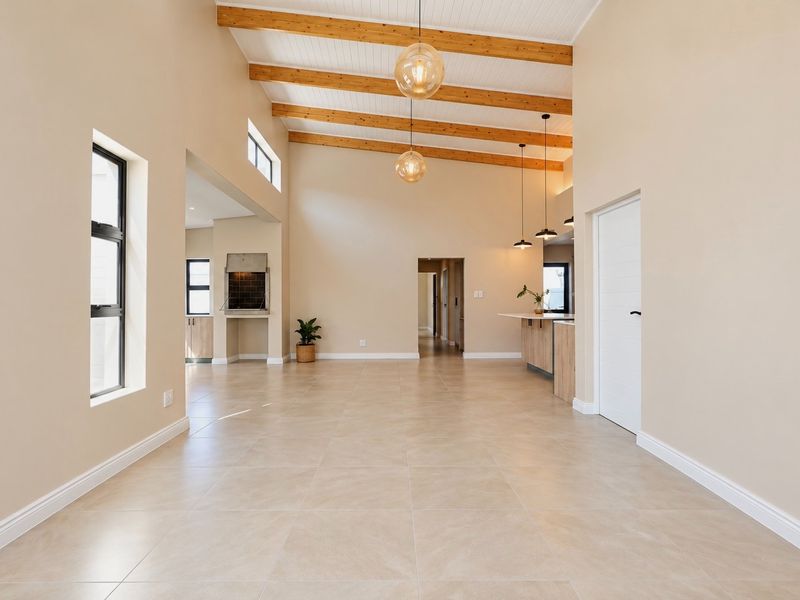 Spacious open-plan living area featuring high ceilings with exposed timber beams, tiled flooring, and a built-in indoor braai, creating a bright and modern atmosphere.