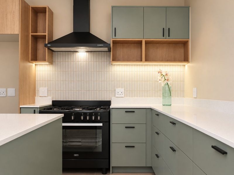 Modern kitchen featuring sage green cabinetry, white quartz countertops, a gas stove with extractor fan, and stylish vertical tiled backsplash with integrated lighting.