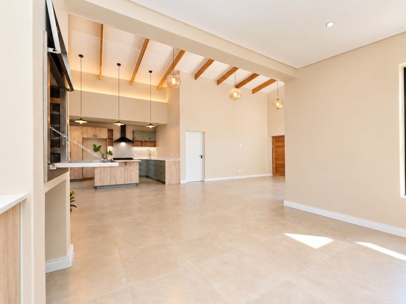 Spacious open-plan living area featuring high ceilings with exposed timber beams, a modern kitchen with island, and a built-in indoor braai.