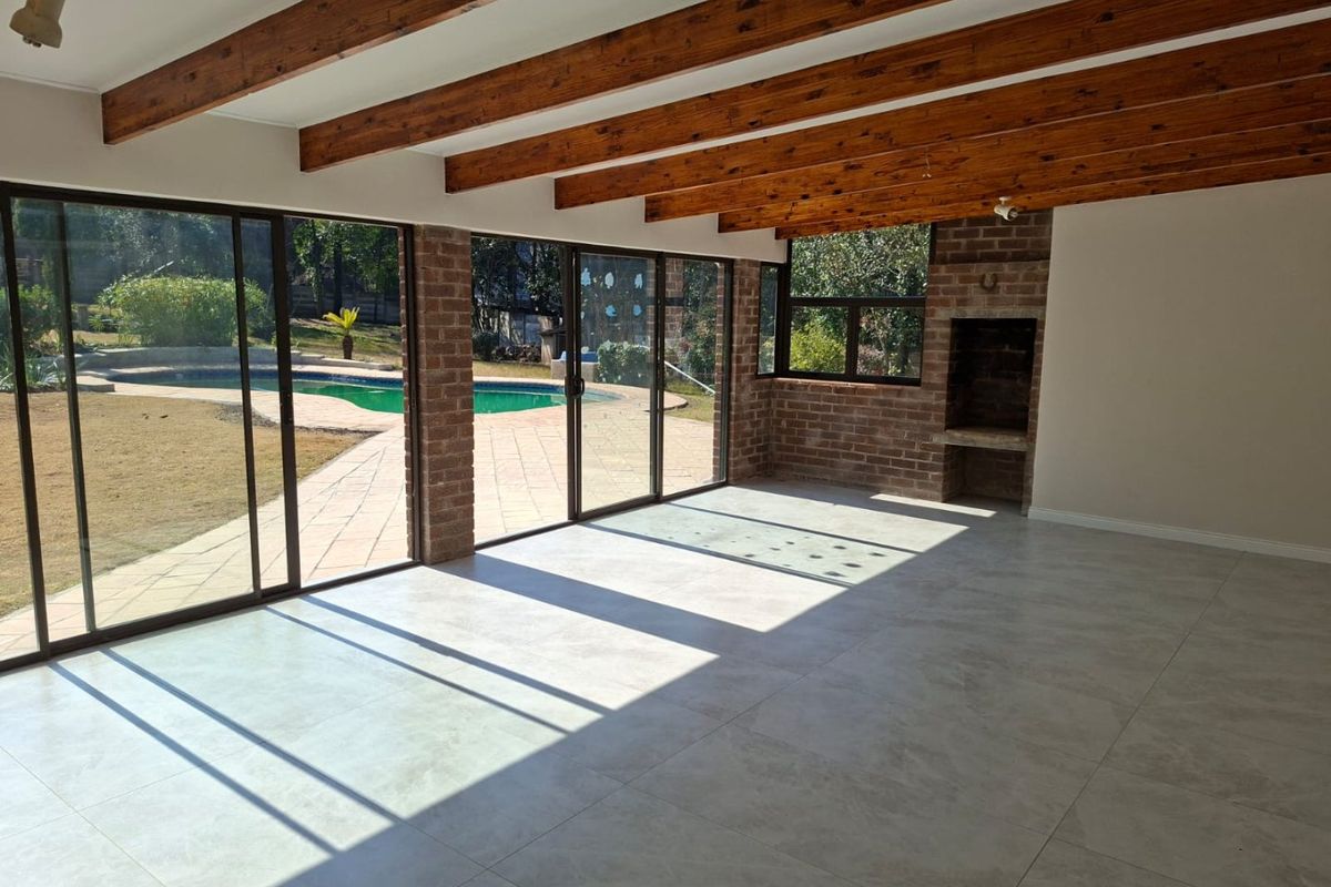 Spacious living area featuring exposed timber beams, tiled floors, and a built-in brick fireplace, with large sliding doors opening to the pool and garden.
