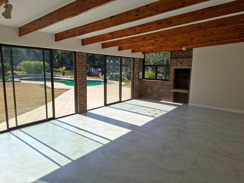 Spacious living area featuring exposed timber beams, tiled floors, and a built-in brick fireplace, with large sliding doors opening to the pool and garden.