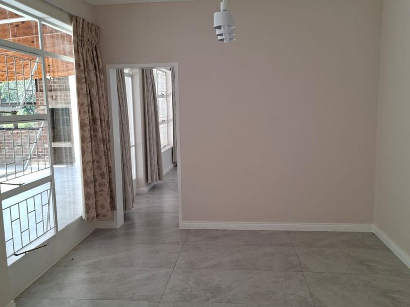 A bright, empty living area featuring large format floor tiles, neutral walls, and a sliding glass door providing access to an outdoor patio space.