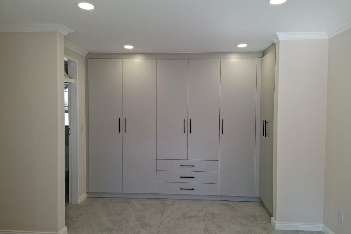 A clean, modern bedroom featuring extensive built-in cabinetry with integrated drawers, neutral tiled flooring, and recessed ceiling lighting.